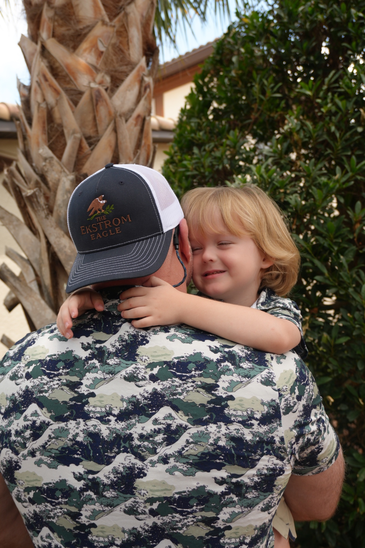 Father in an Ekstrom Eagle wave-print polo and cap holding his smiling son